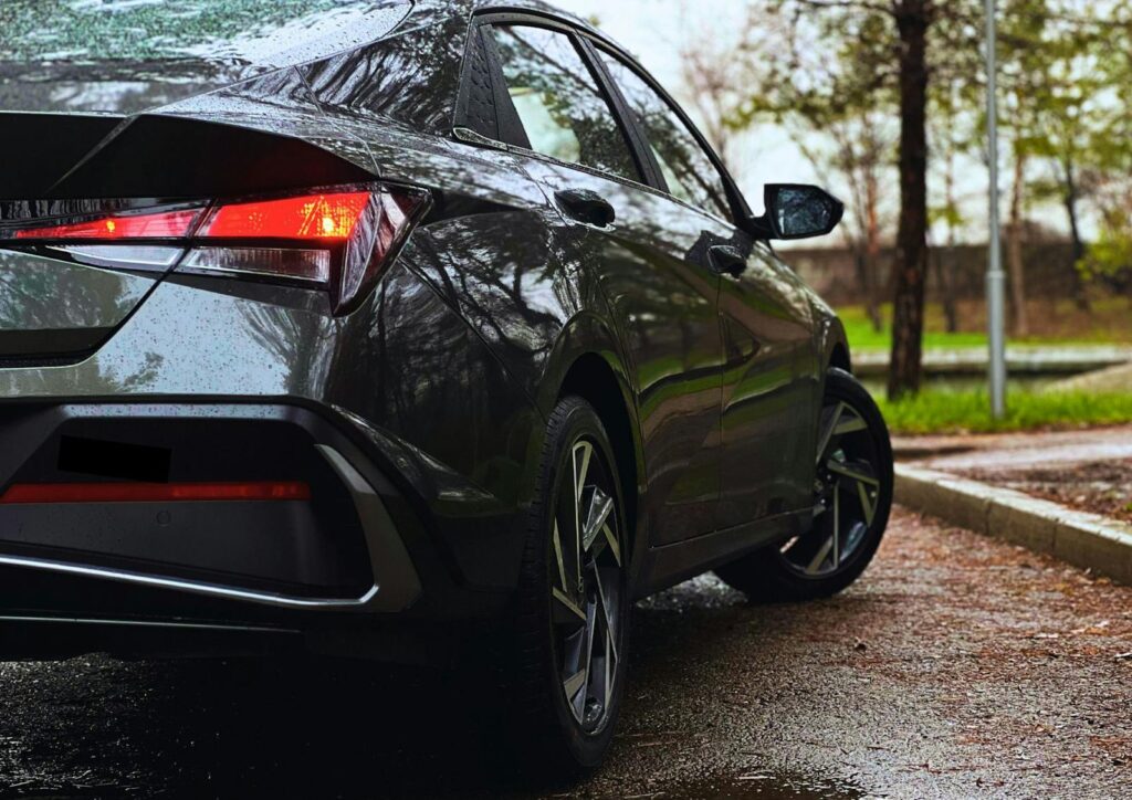 Rear view of a modern car on a rainy day, parked on a wet road surrounded by trees.