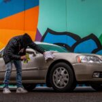 man in black jacket and blue denim jeans standing beside silver car